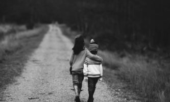 Två barn går längs en väg med armarna runt varandra.